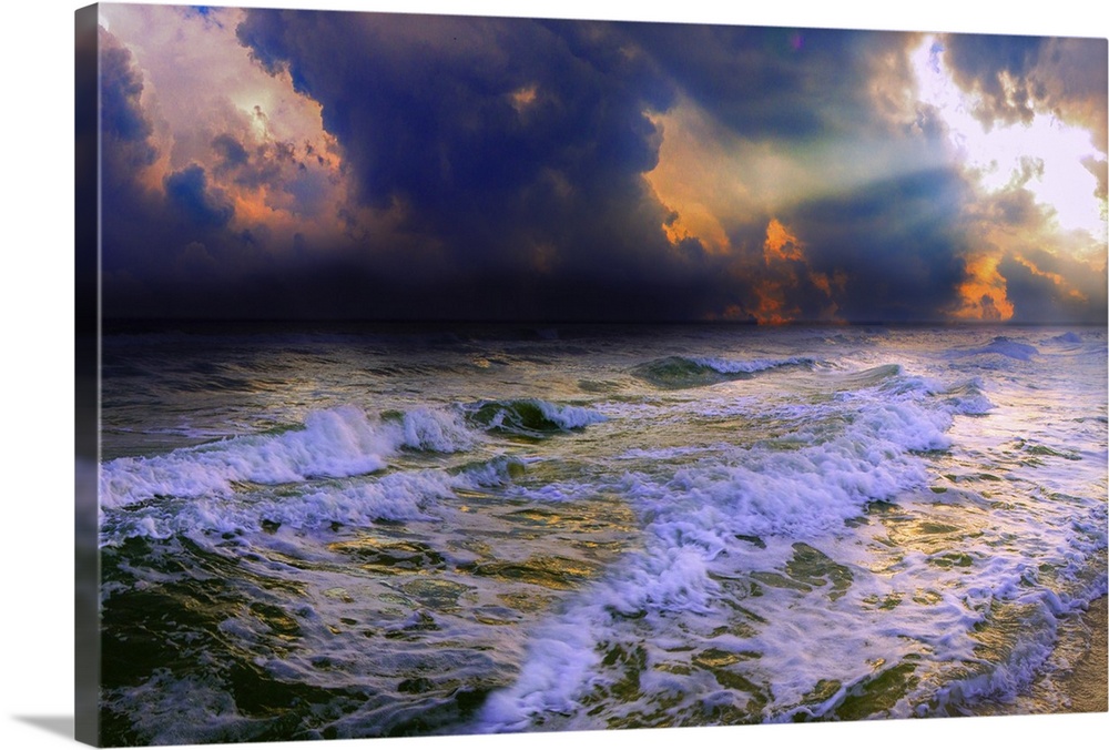 Sun rays break through dark blue clouds on a stormy night over a dark ocean and waves.