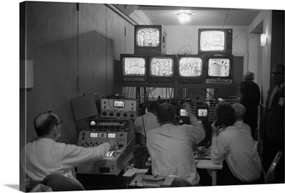 Broadcasting technicians, seated in front of bank of television sets