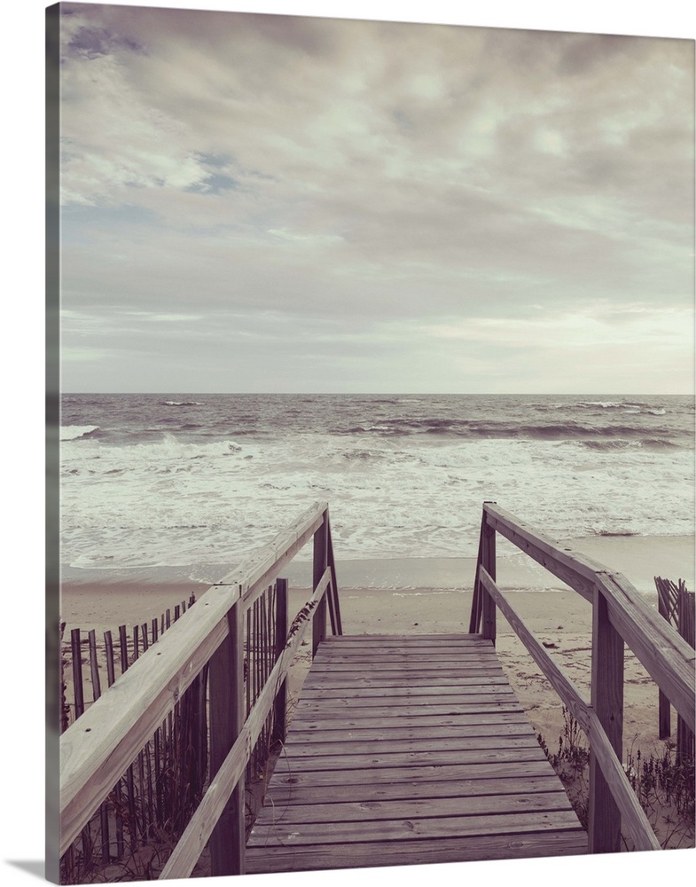 Photograph, with a faded look, of a wooden boardwalk that leads to the ocean shore.