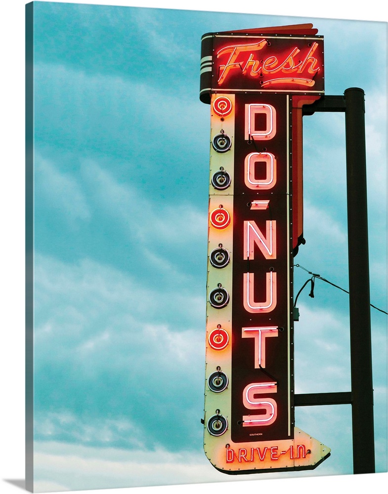 Photograph of a vintage 'Fresh Doughnut' neon sign with a cloudy blue sky in the background.