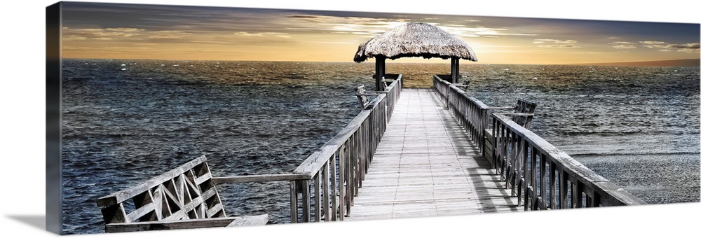 Panoramic photo of a pier reaching out to the sea with a thatched roof near the horizon.