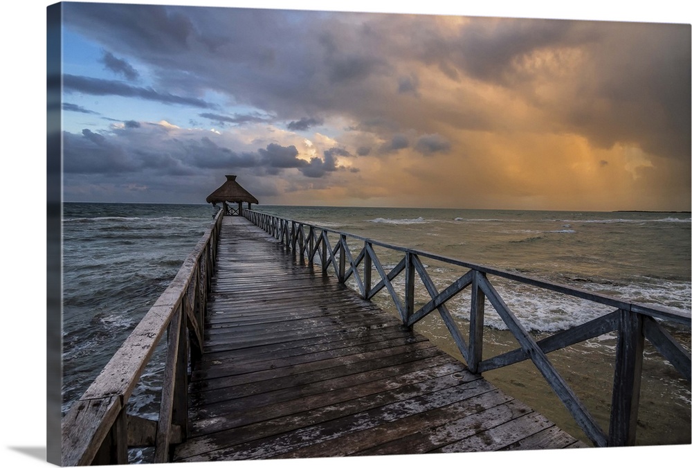 Photograph of a dock over the ocean with an orange cloudy sunset.