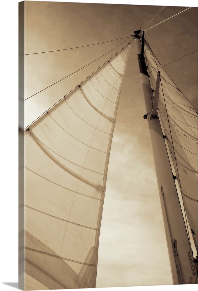 Vertical, low angle photograph, looking up large sails as the sun shines through them, against a partly cloudy sky.