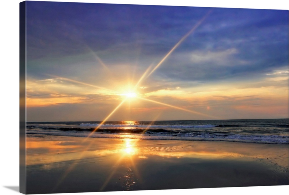 The sunrises over the ocean and reflects on the waves of a sandy beach in this landscape photograph.