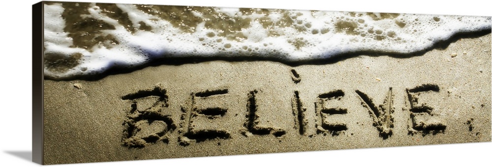 The word "Believe" drawn in the sand near the ocean water.