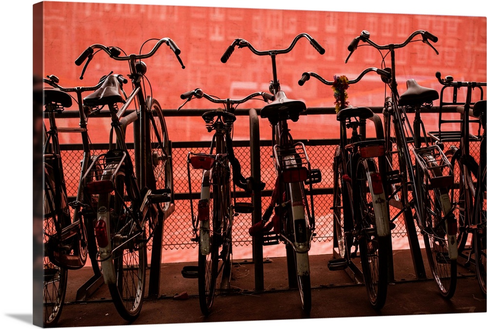 Several bicycles parked along a railing in front of a red wall.