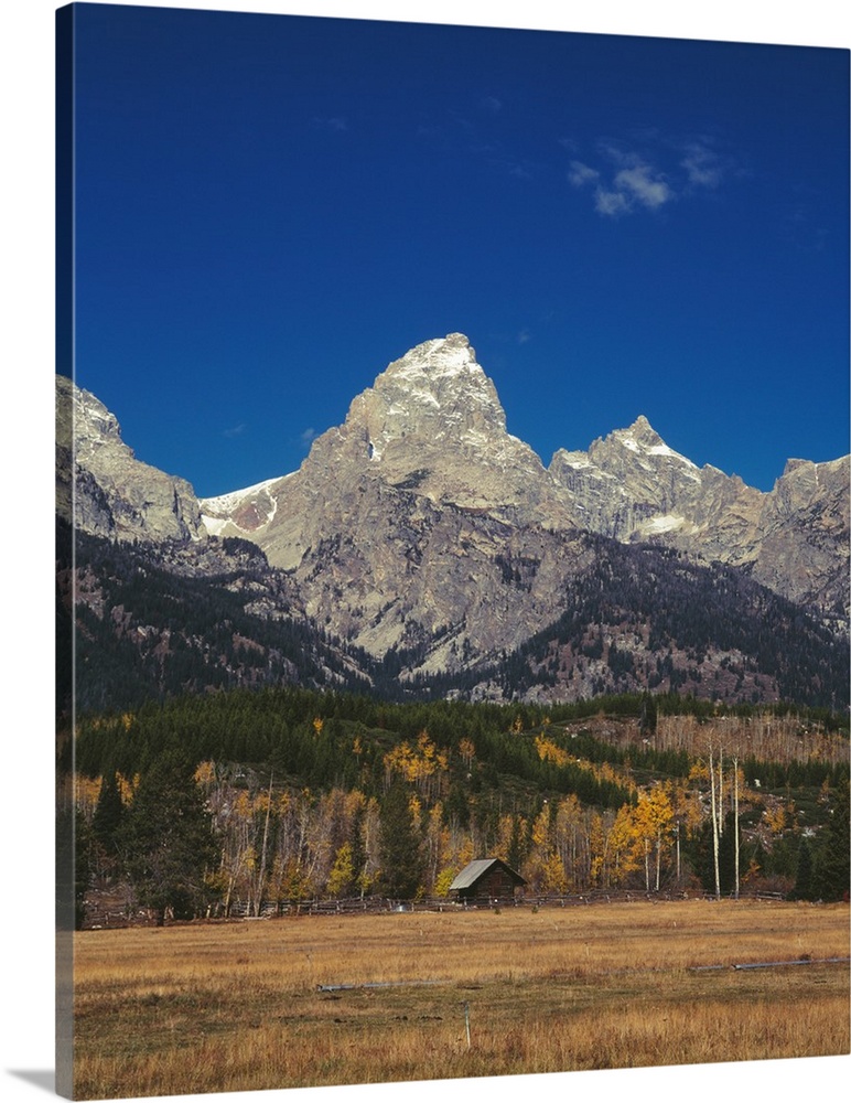 Landscape photograph of the Grand Teton mountain range with a small log cabin in the foreground.