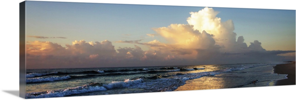 Panoramic photograph of the ocean at sunrise with fluffy clouds in the sky and shorebirds in the water.