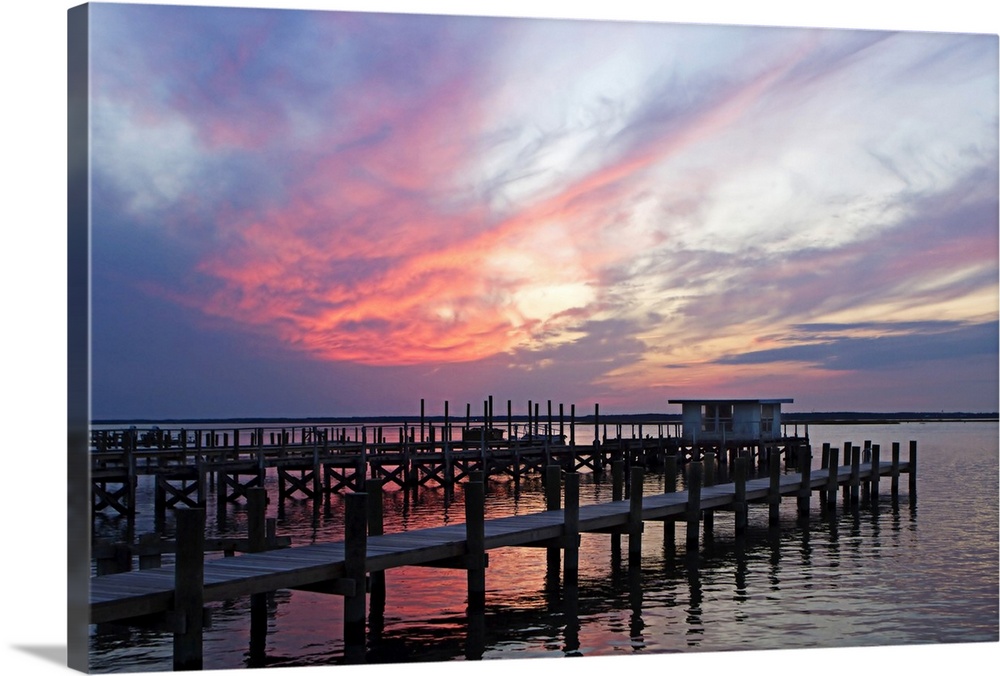 Landscape photograph on a big wall hanging of several docks lined next to each other, in calm waters, beneath a sky of pas...