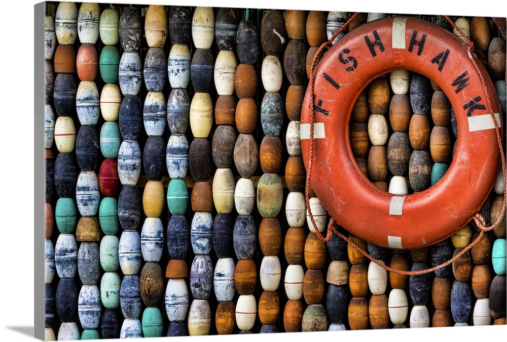 A collection of fishing buoys and a large red lifering on a wall.