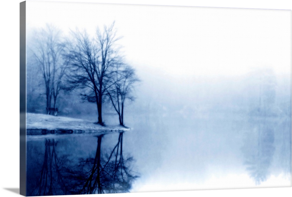 A photograph taken of a lake with bare trees off to the left side and more trees behind dense fog toward the back of the l...