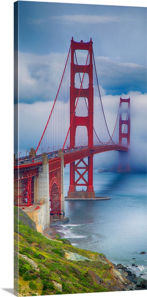 Tall photograph of a green coast and the Golden Gate bridge with thick fog.
