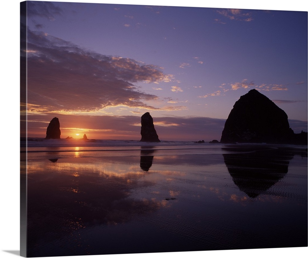 Silhouetted photograph of Haystack Rock during a purple and orange sunset.