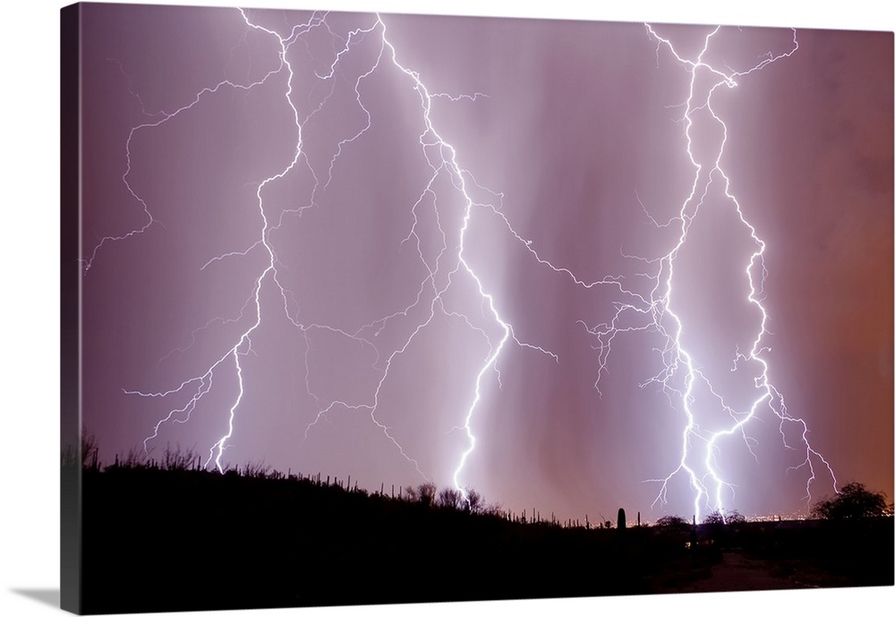 Photograph of three large lightning bolts striking down in an orange, purple, and pink sky above a desert in Arizona.