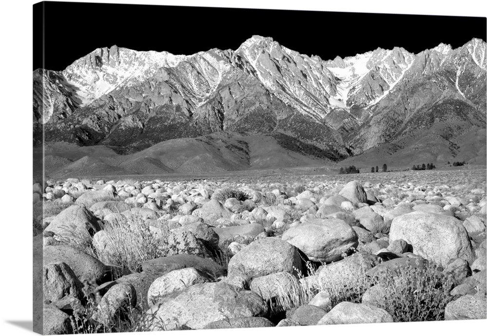Black and white photograph of rock covered ground leading to snowy mountain peaks in the background.