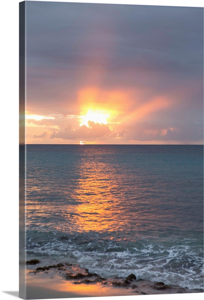 Vertical photograph of a sunset beaming though clouds over a blue ocean.