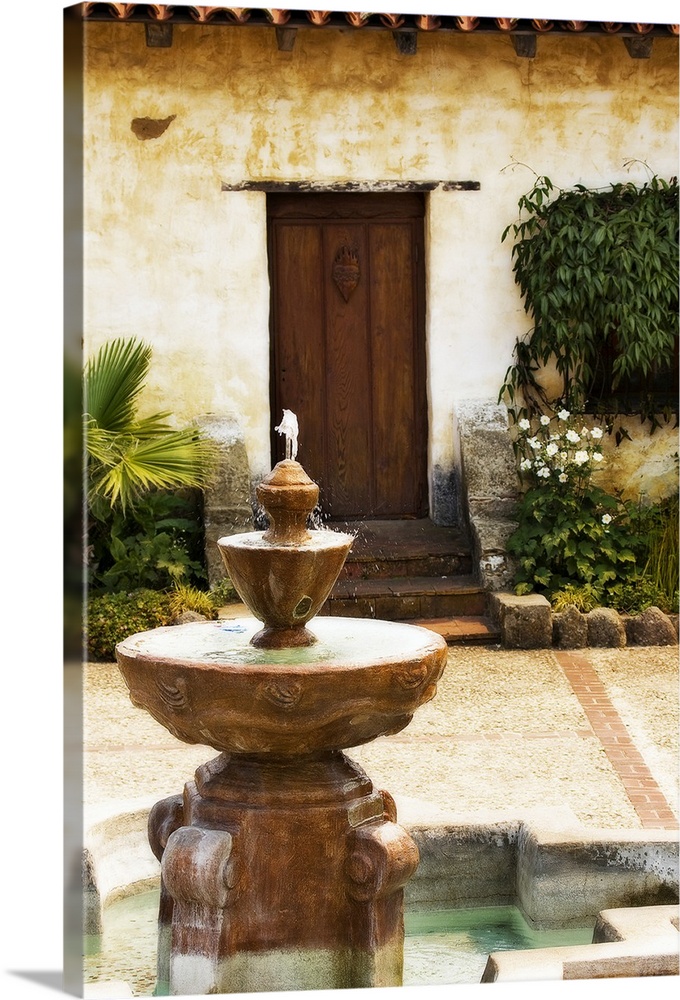 Photograph fountain with stone house and wooden door in background.