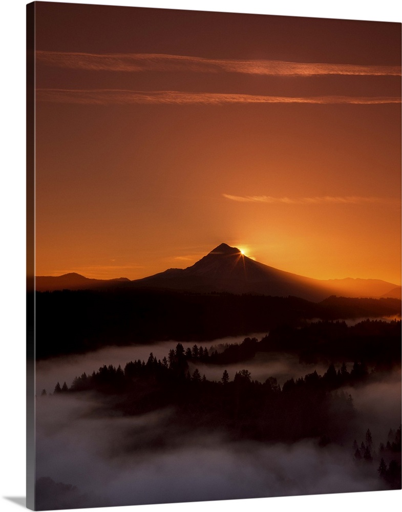 The sun setting behind Mount Hood, with dense fog in the valley below.