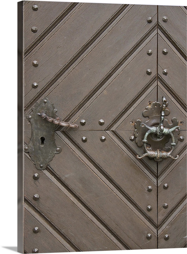 Close up of a wooden door with a diamond pattern and an iron knocker.