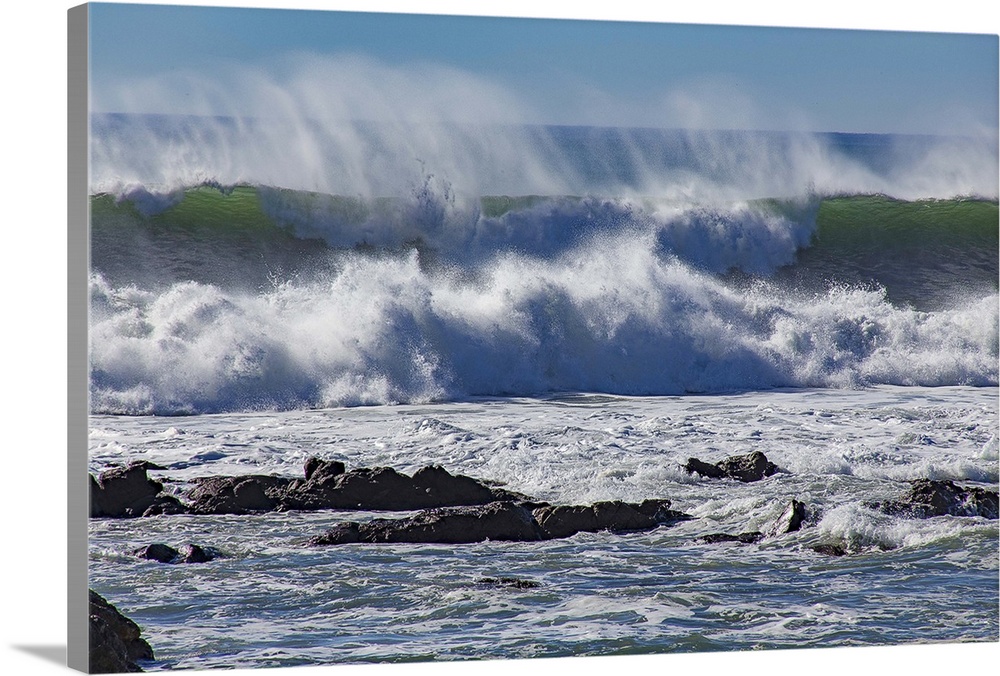 Photograph of a big dramatic wave crashing over rocks in North Cayucos, California.