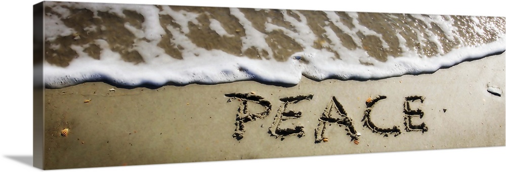 The word "Peace" drawn in the wet sand near ocean water.