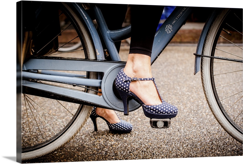 A woman in dotted high heels stepping onto the a bike pedal.