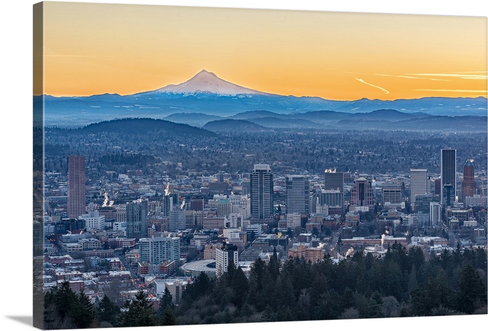 Photograph of the city of Portland with rolling hills and Mt. Hood in the background, and an orange sunset above.