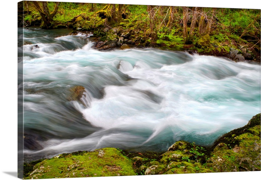 Long exposure photograph of a rushing river surrounded by bright green vegetation.
