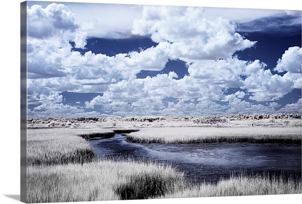 Cool toned photograph of a deep blue river winding through a marsh with beautiful, white, fluffy clouds in the sky.