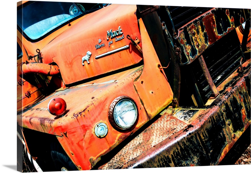 Photograph of an old, rusted, orange Mack truck from a unique angle.