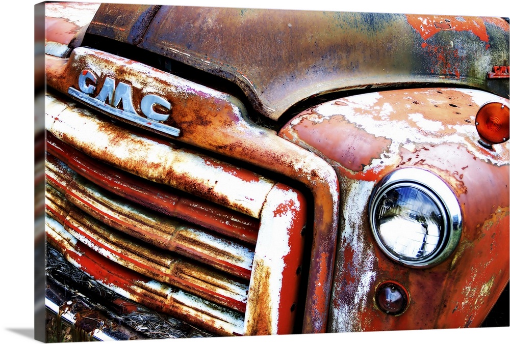 Photograph of the front of an old, rusted, orange GMC truck.