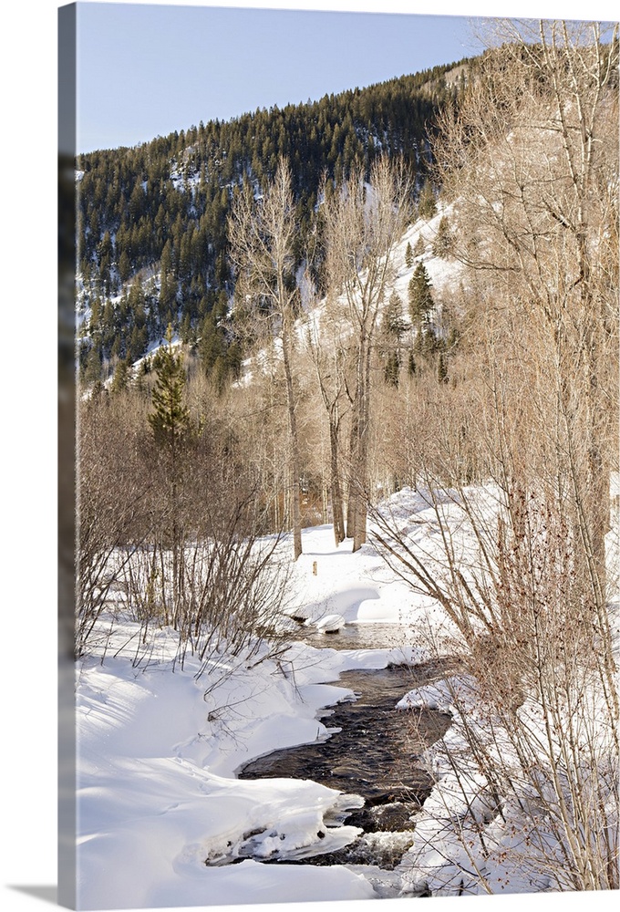 Photograph of a small stream flowing through a snowy mountain landscape.