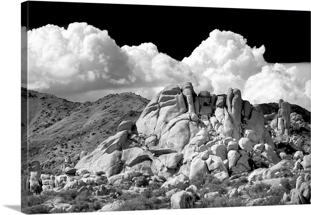 Black and white photograph of canyon rocks with rolling hills in the background and white fluffy clouds in the sky.