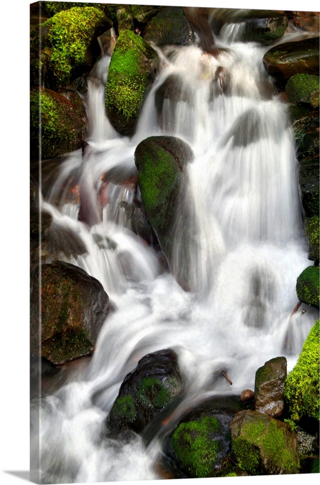 Long exposure photograph of a waterfall over bright, mossy, green rocks.
