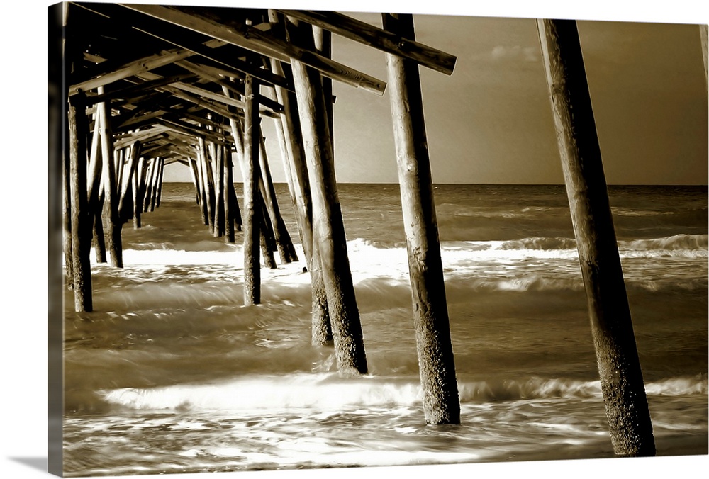 Photograph underneath a wooden pier with waves rolling in.