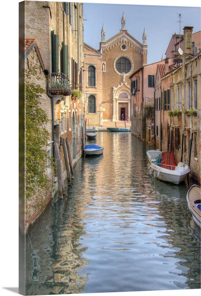 HDR photograph of a canal flowing through the alleys of Venice, Italy, with small boats floating moored to the edge.