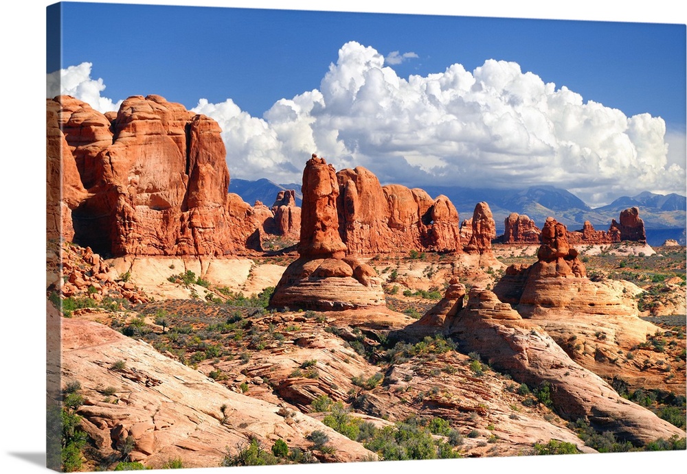 Landscape photograph of sandstone rock formations in the desert with fluffy white clouds in the sky.