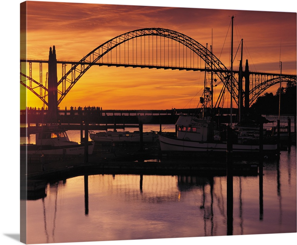 Sunset photograph with silhouetted boats on the Yaquina Bay with a bridge in the background.
