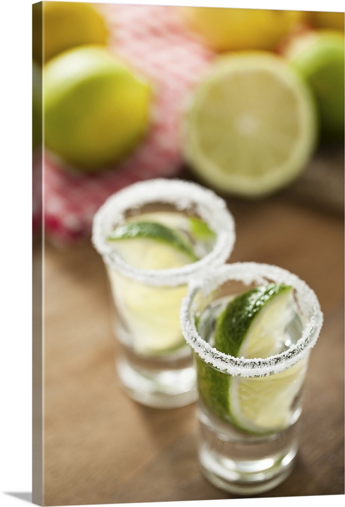 2 Shot-glasses filled with silver tequila, decorated with limes and sea-salt. limes and citrons in background.
