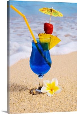 A Blue Hawaii tropical cocktail on the beach, wave washing on the sand.