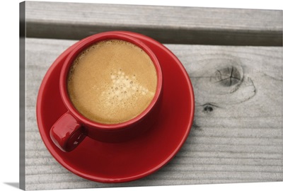A bright red cup of espresso coffee on a picnic table outdoors on a summer day.