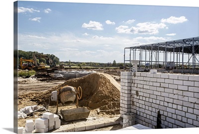 A cement mixer and brick wall in front of a construction frame at a construction site