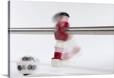 A foosball figurine kicking a soccer ball, blurred motion