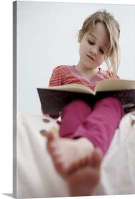 A four-year-old girl reads a book while sitting on her bed