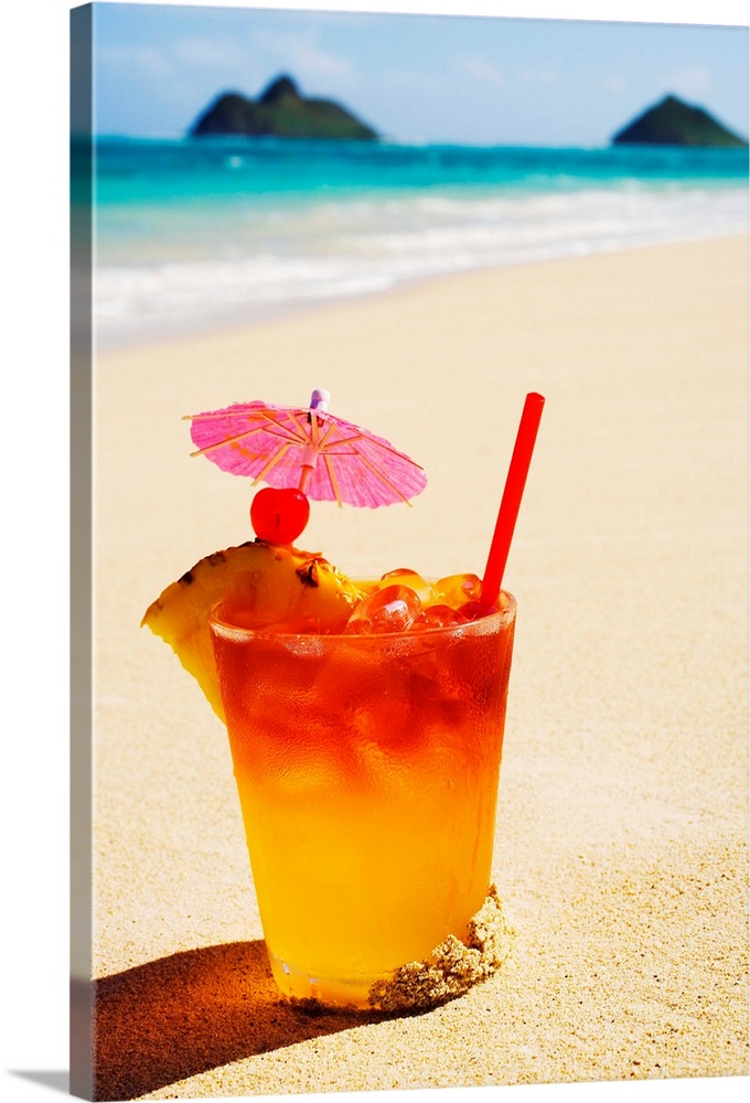 A mai tai garnished with pinapple and a cherry, sitting in the sand on the beach.