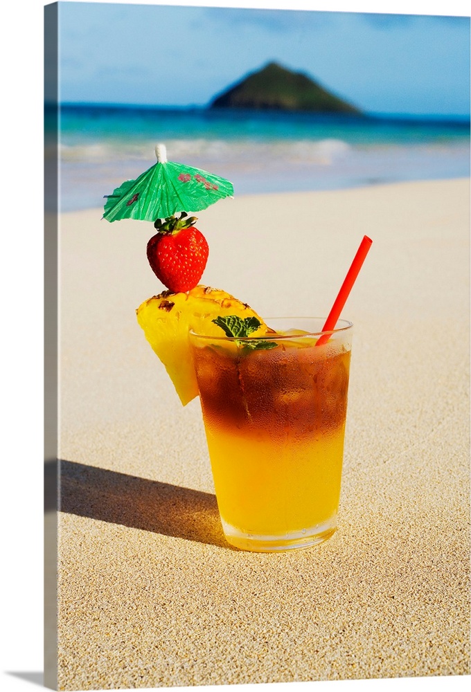 A mai tai garnished with pinapple and a strawberry, sitting in the sand on the beach.