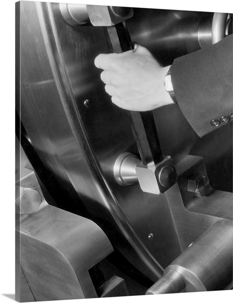 A disembodied hand grasp the handle of a large bank vault and pushes it closed. Undated photograph.