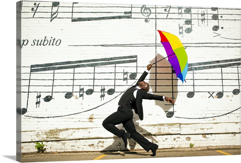 A young man jumping and dancing with an umbrella outside in front of a wall with musical notes on it.