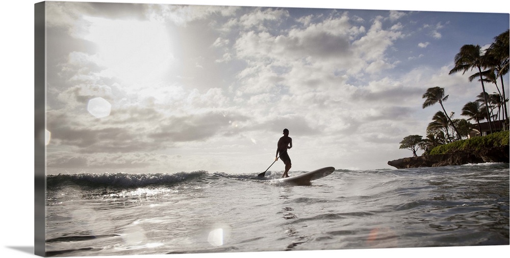 Silhouette of a young man catching an ocean wave on a stand up paddle board, wide