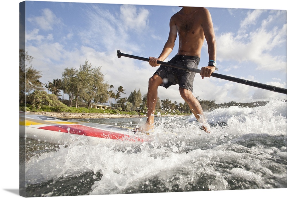 Low angle view of a young man riding an ocean wave on a stand up paddle board